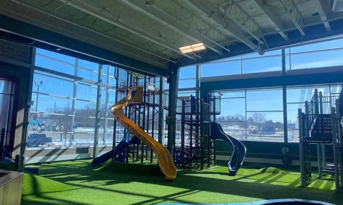 Indoor play area at 2|42 Community Center in Ann Arbor, featuring large slides and climbing structures with natural light streaming through floor-to-ceiling windows.