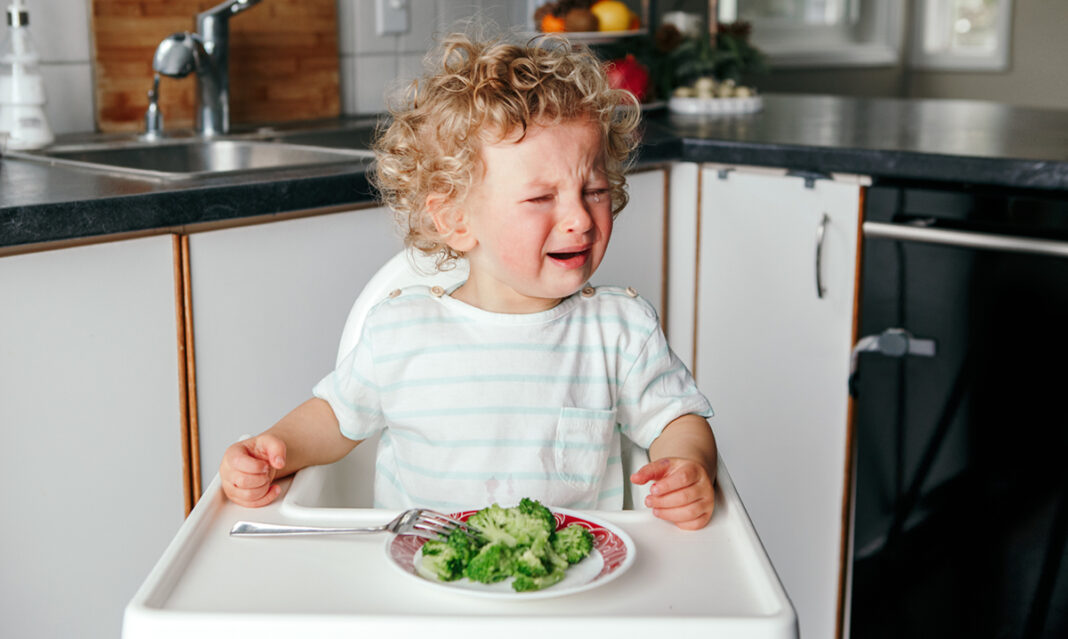 Toddler crying with a bowl of broccoli