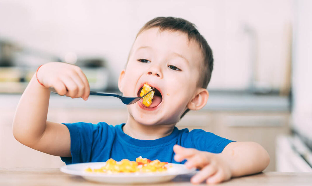 Little boy enjoying a big bite of food and displaying the benefits of breakfast for kids.