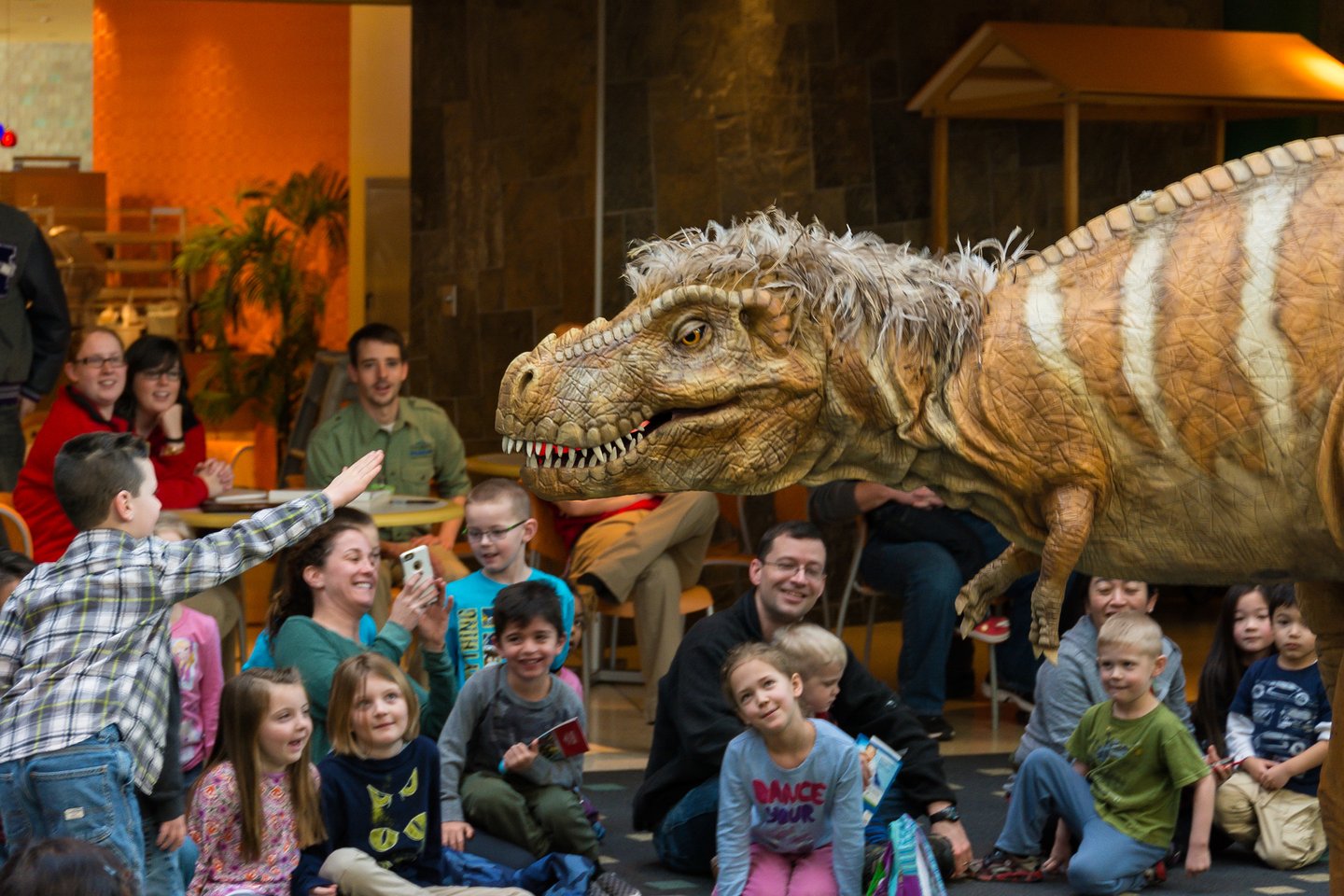 Children and families interact with a life-size dinosaur puppet during a lively show at the Children’s Museum of Indianapolis.