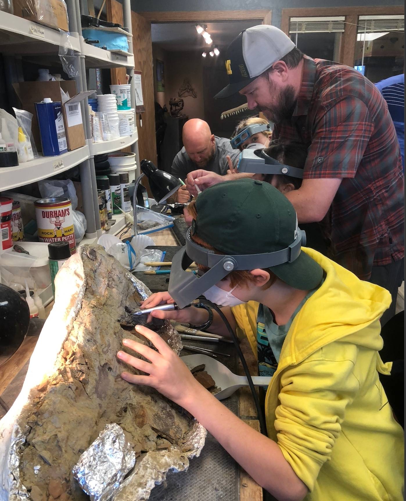 Child and adults carefully work on cleaning a large dinosaur fossil at the Dinosaur of the Hell Creek Museum in South Dakota.