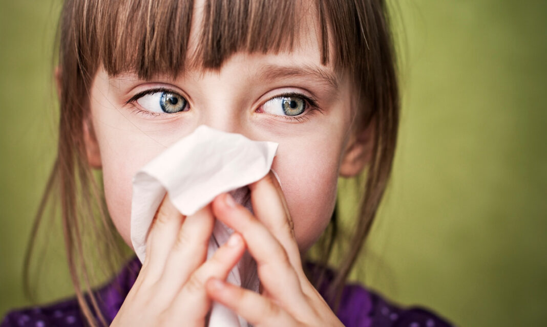 A young girl wipes her nose with a tissue, highlighting the eczema and allergy connection in children. Allergies can often trigger eczema flare-ups in kids.