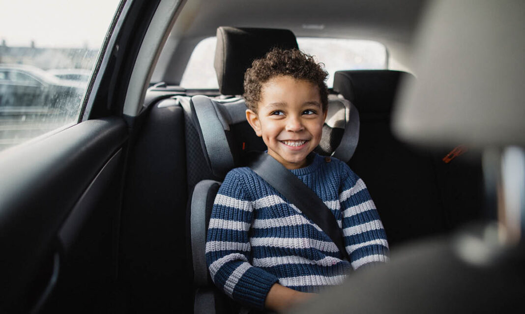 A happy child sits securely in a car seat with a seatbelt, smiling while riding in the back of a vehicle. Car seat safety is essential for protecting young passengers.
