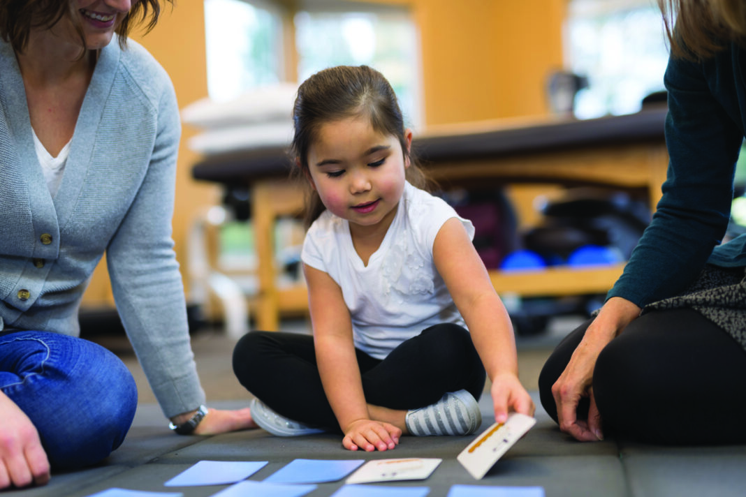 An occupational therapist works with a kindergarten-age ethnic girl on fine motor and coordination skills