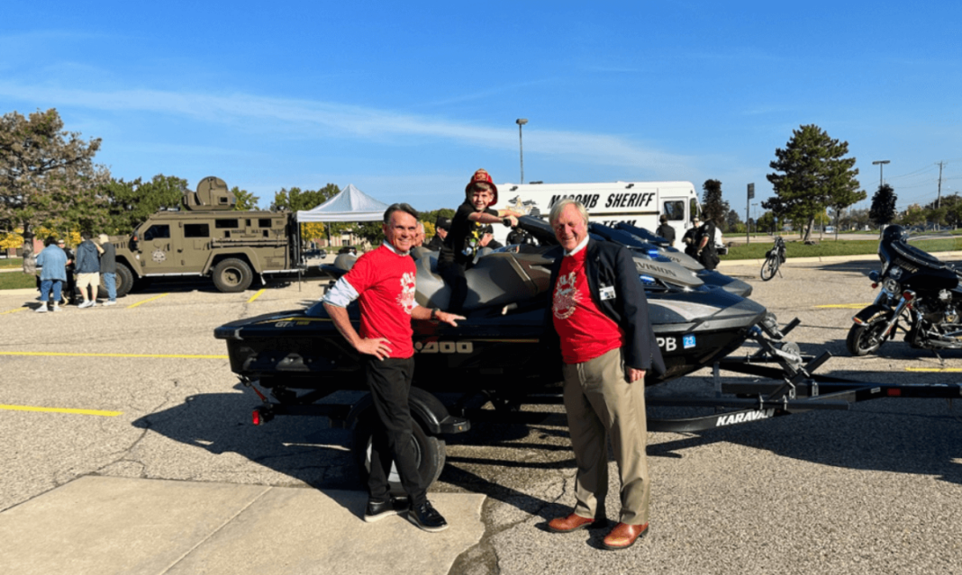 Two men and a child smiling in front of a vehicle that's part of the touch-a-truck experience at the Special Education Expo in Macomb County