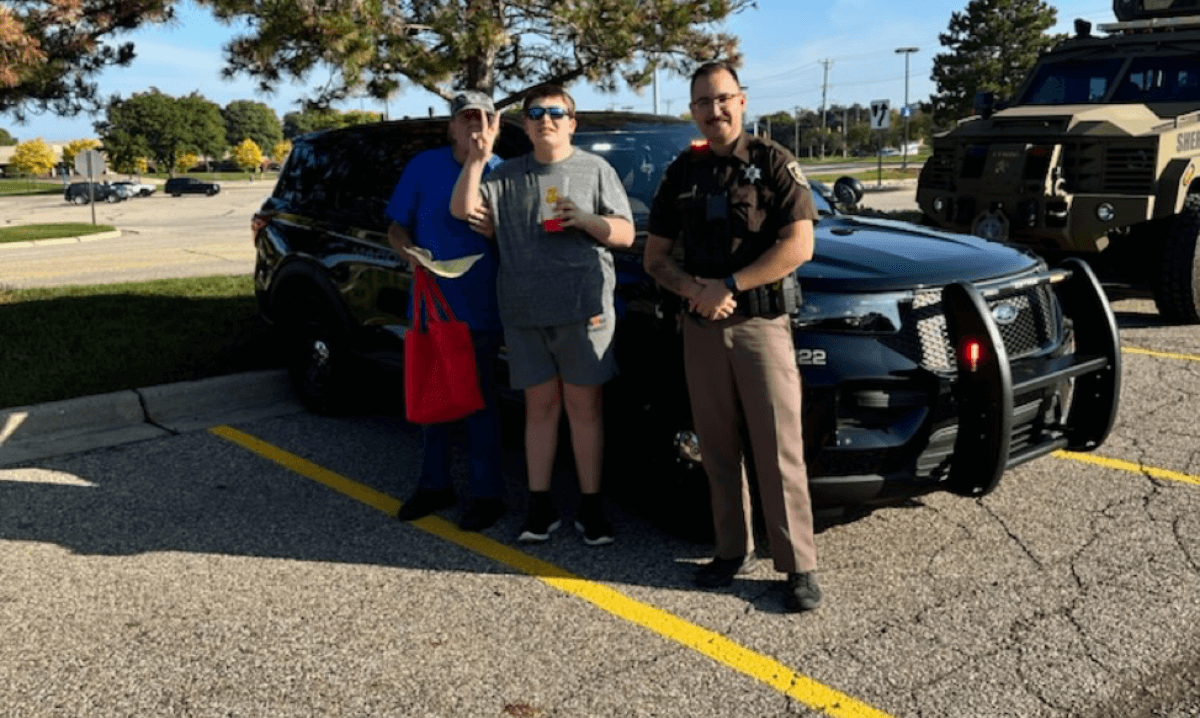 Attendees at the Special Education Expo in Macomb County smile with a police officer by a police vehicle, part of the touch-a-truck experience.