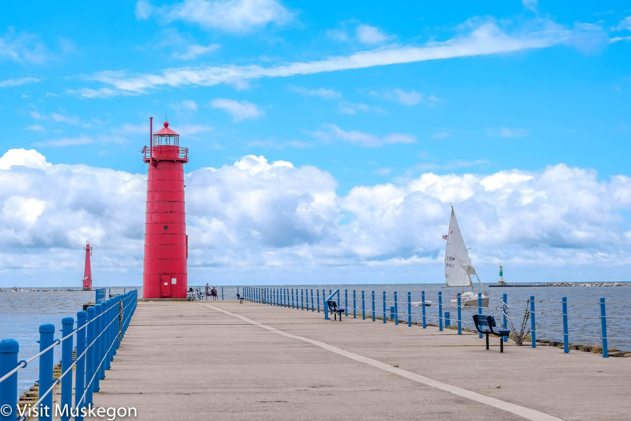 a photo of a red lighthouse at the end of a road on a coast area