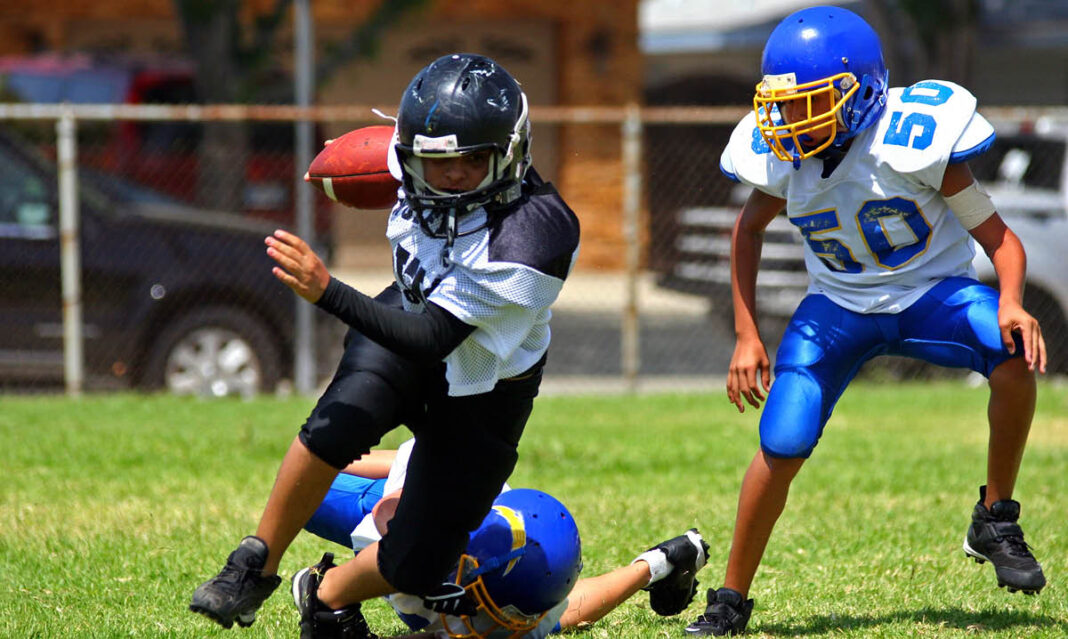 Youth football players compete in a game, highlighting the risk of concussions in student athletes. Proper helmets and tackling techniques are essential for injury prevention.