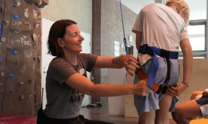 Helping children climbing up with harness in YMCA