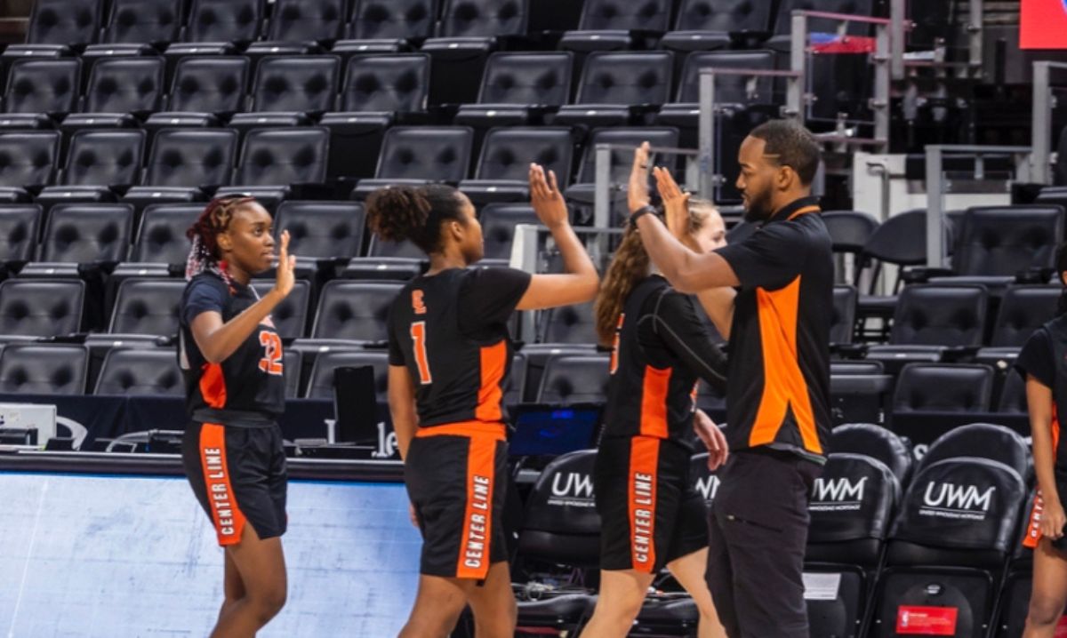 Coach Josh Banks high-fives girls basketball players during a game in Macomb County, promoting youth sports and community living.