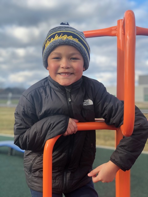 A young boy smiling on the playground at Achieve Charter Academy, highlighting student engagement and scholarship opportunities.