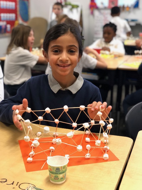 A student proudly displaying a STEM project made with marshmallows and toothpicks at Achieve Charter Academy, promoting hands-on learning and scholarships.