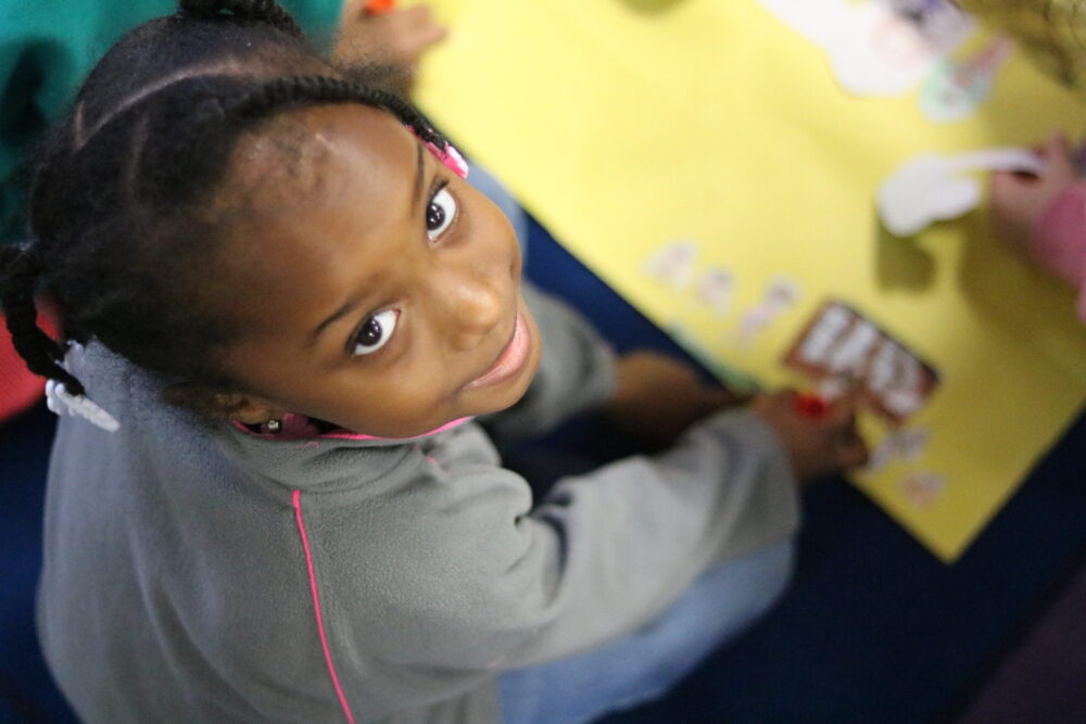 A young student smiling while participating in a creative classroom activity at Achieve Charter Academy, highlighting scholarship programs.