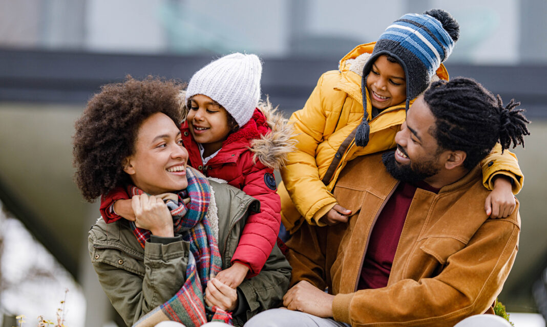 A cheerful family spending quality time together outdoors during a meaningful holiday, dressed warmly in winter coats, scarves, and hats.