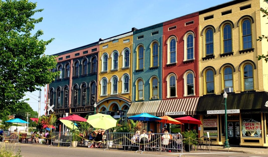 A row of colorful historic downtown buildings in Ann Arbor with outdoor seating and vibrant umbrellas, creating a family-friendly atmosphere for dining and strolling.