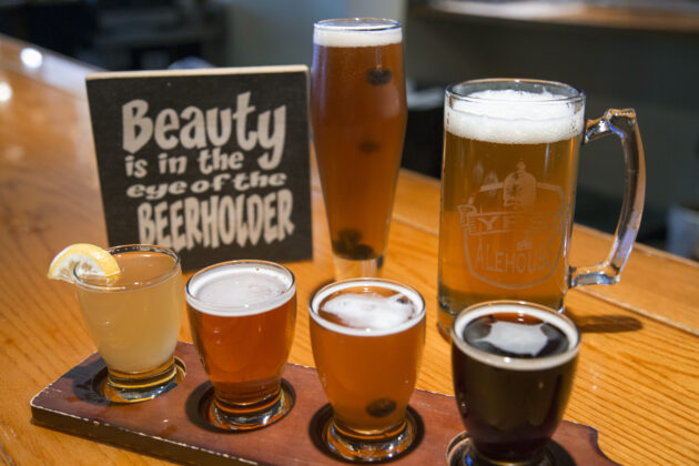 A selection of craft beers at a tasting flight in Ann Arbor with a sign reading "Beauty is in the eye of the beerholder," showcasing a unique and family-friendly local brewery.