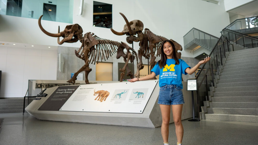 A smiling student greets visitors at the University of Michigan Museum of Natural History, with prehistoric skeletons and interactive exhibits that create a family-friendly educational experience.