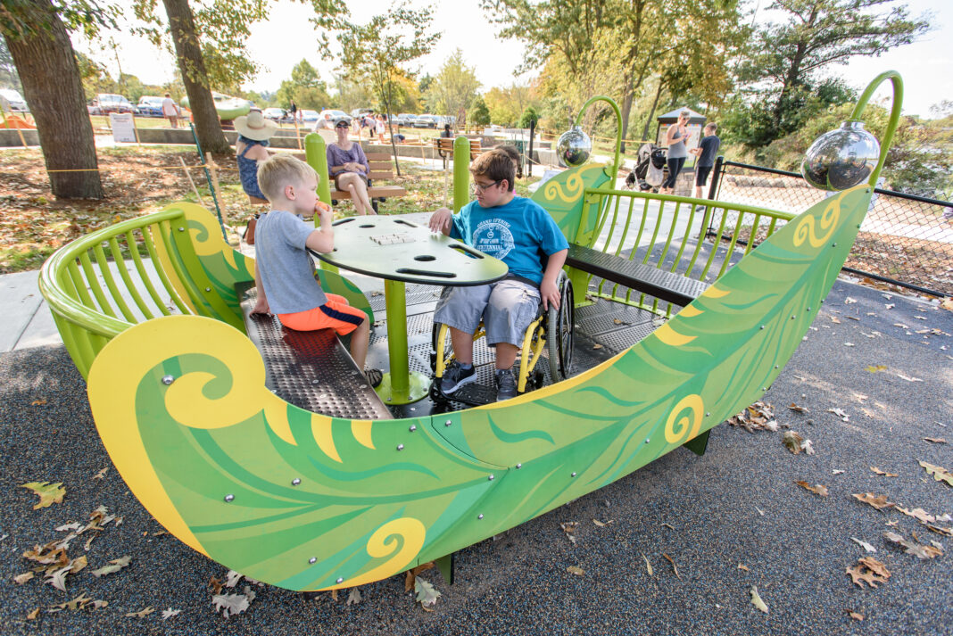Children playing on an inclusive green playground structure in Ann Arbor, designed for accessibility and family fun for kids of all abilities.