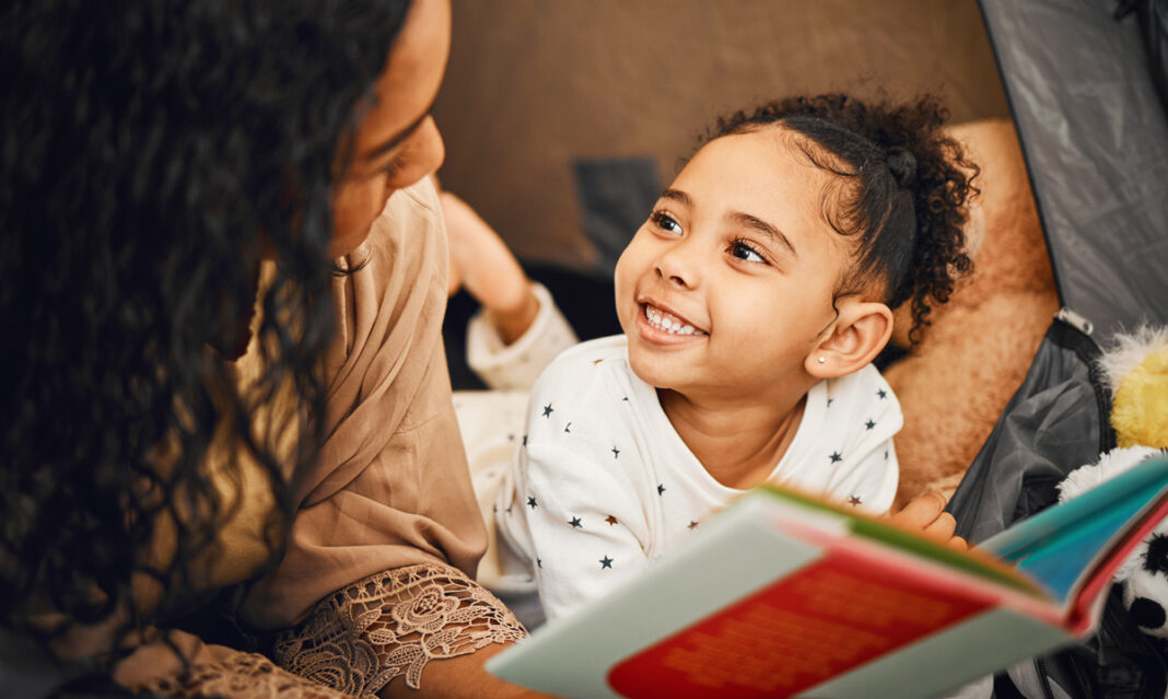 A smiling young girl and her mother reading a book together, illustrating the impact of books on children's literacy and fostering a love for learning.