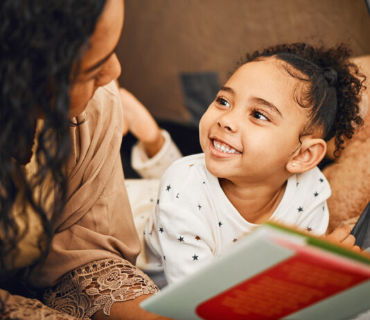 A smiling young girl and her mother reading a book together, illustrating the impact of books on children's literacy and fostering a love for learning.