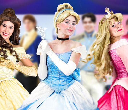 Three performers dressed as princesses—Belle, Cinderella, and Aurora—smile and pose at a magical Royal Princess Ball event. Behind them, characters dressed as princes add to the enchanting atmosphere. This family-friendly event brings beloved fairytale characters to life for an unforgettable experience.