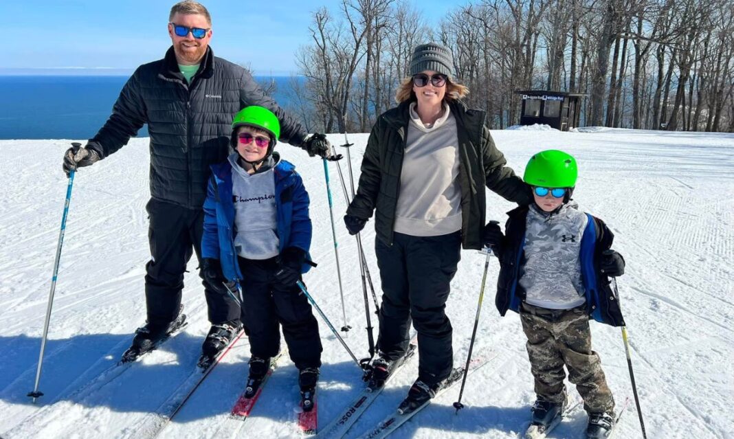 A family of four posing on a sunny ski slope at Mont Ripley, with Lake Superior in the background, enjoying a winter day of skiing and outdoor fun.