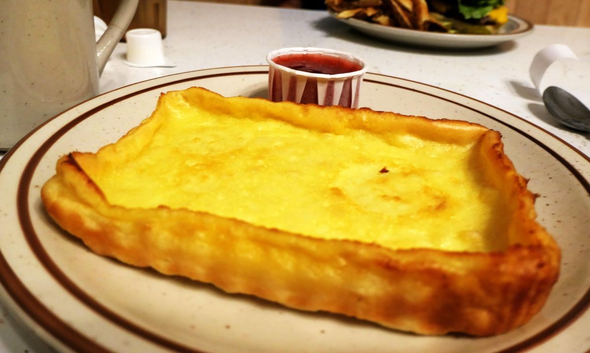 A golden-brown Finnish pancake served on a plate with a side of berry syrup, showcasing a traditional Nordic breakfast dish.