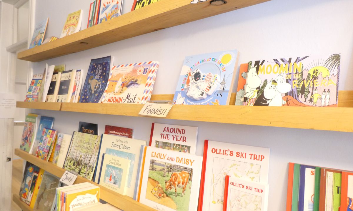 A wooden shelf displaying a vibrant collection of Finnish books, including Moomin titles and children's literature, at North Wind Books, highlighting Nordic storytelling and culture.