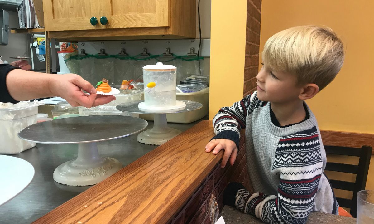 A young boy eagerly watching as a baker decorates a cupcake with colorful frosting at Roy’s Pasties and Bakery.