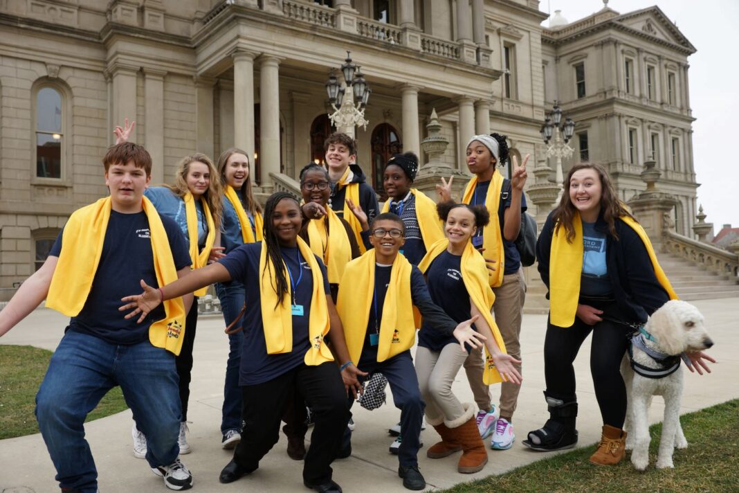 A diverse group of students wearing yellow scarves posing in front of the Michigan Capitol, celebrating charter schools in Michigan.