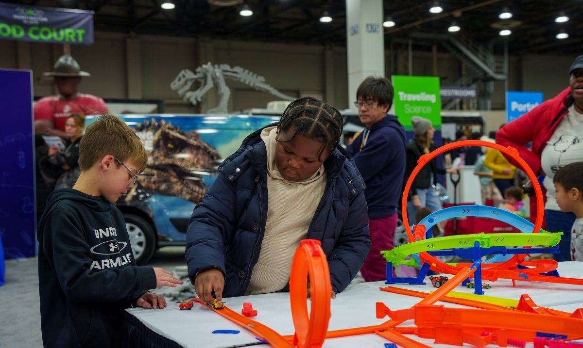 Children playing with toy car tracks at the Detroit Auto Show, highlighting family-friendly activities for kids.
