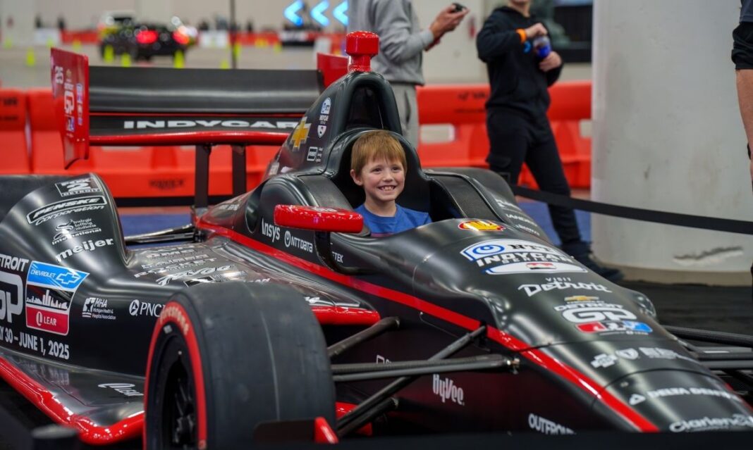 A young child smiling while sitting in an IndyCar at the Detroit Auto Show, showcasing a fun family activity with kids.