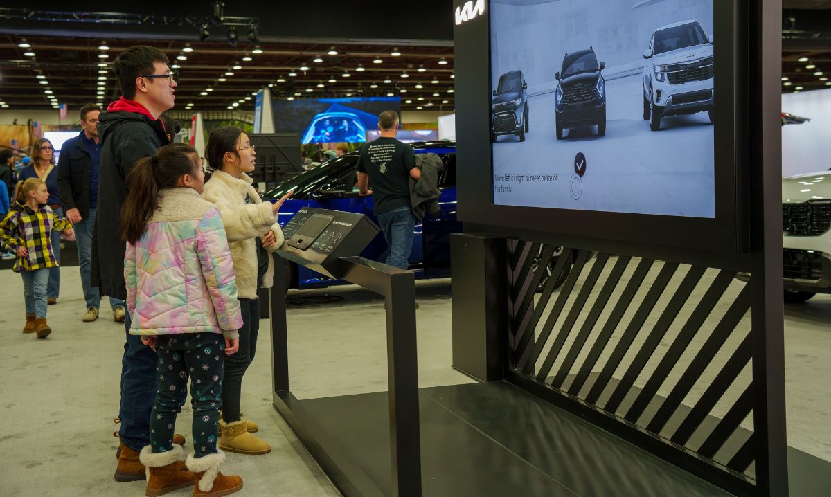 A family exploring an interactive car display at the Detroit Auto Show, offering engaging experiences for kids and adults alike.