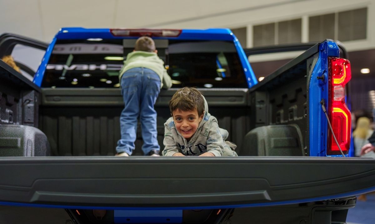 Children playing in the bed of a pickup truck at the Detroit Auto Show, showcasing interactive experiences for kids.