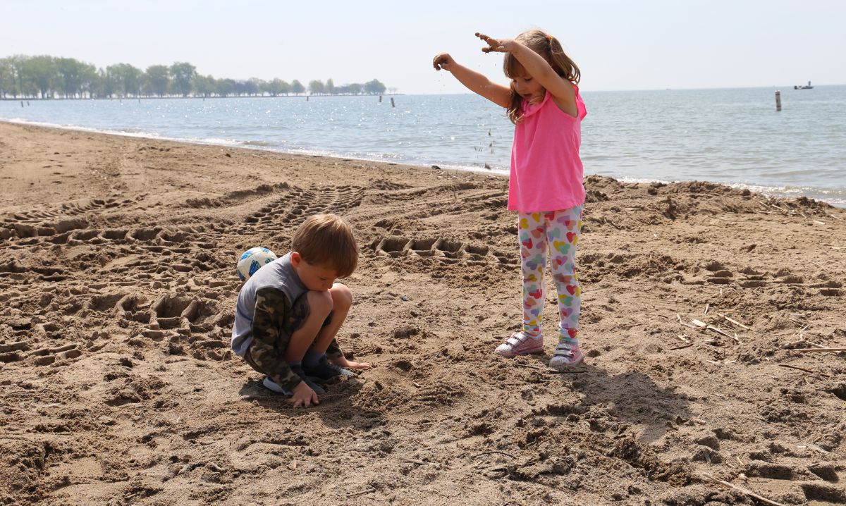 Two young children playing in the sand on a sunny beach at Lake St. Clair Metropark in Macomb County, showcasing one of the free things to do with kids in the area.