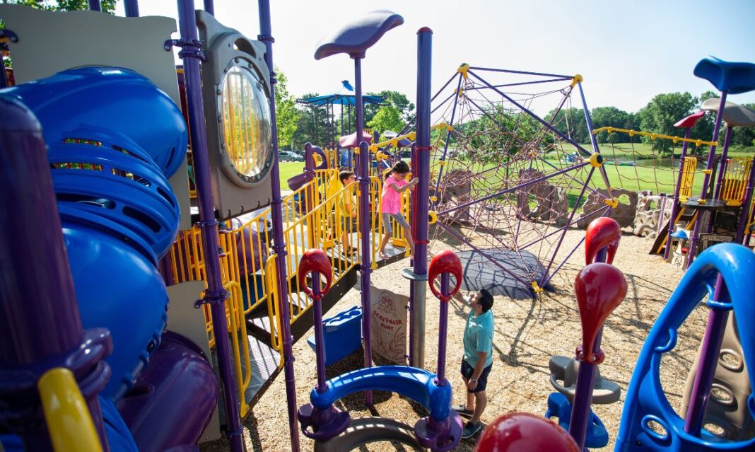 Children playing on a colorful playground with climbing structures, slides, and a spider-web rope design at Stony Creek Metropark in Macomb County, highlighting one of the free things to do with kids in the area.
