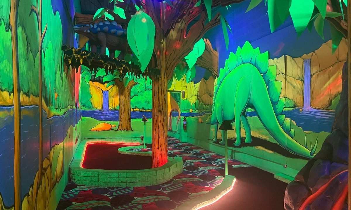 Dinosaur-themed indoor mini golf course at Zap Zone in metro Detroit with glowing lights and colorful prehistoric decorations.