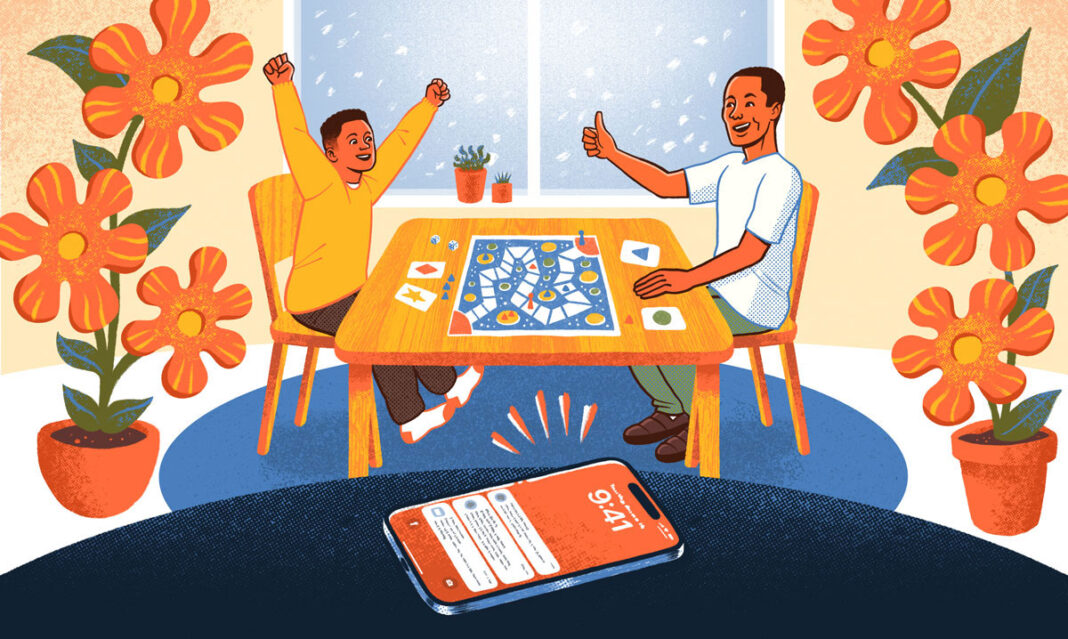 A cheerful parent and child enjoying a board game together at a wooden table, illustrating mindful parenting and quality family time, with a phone set aside on silent mode in the foreground. Bright orange flowers and a snowy window in the background create a warm, focused atmosphere.