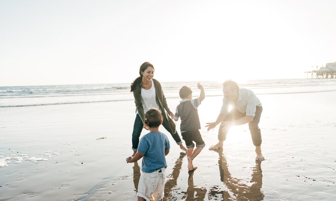 A cheerful family of four playing together on the beach during sunset, enjoying quality time by the ocean with the warm sunlight in the background.