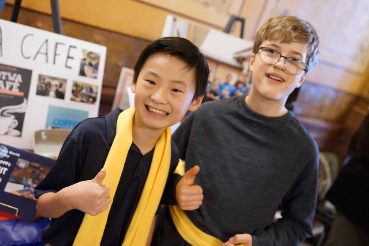 Two smiling students at a charter school event in Michigan, wearing yellow scarves and giving a thumbs up.