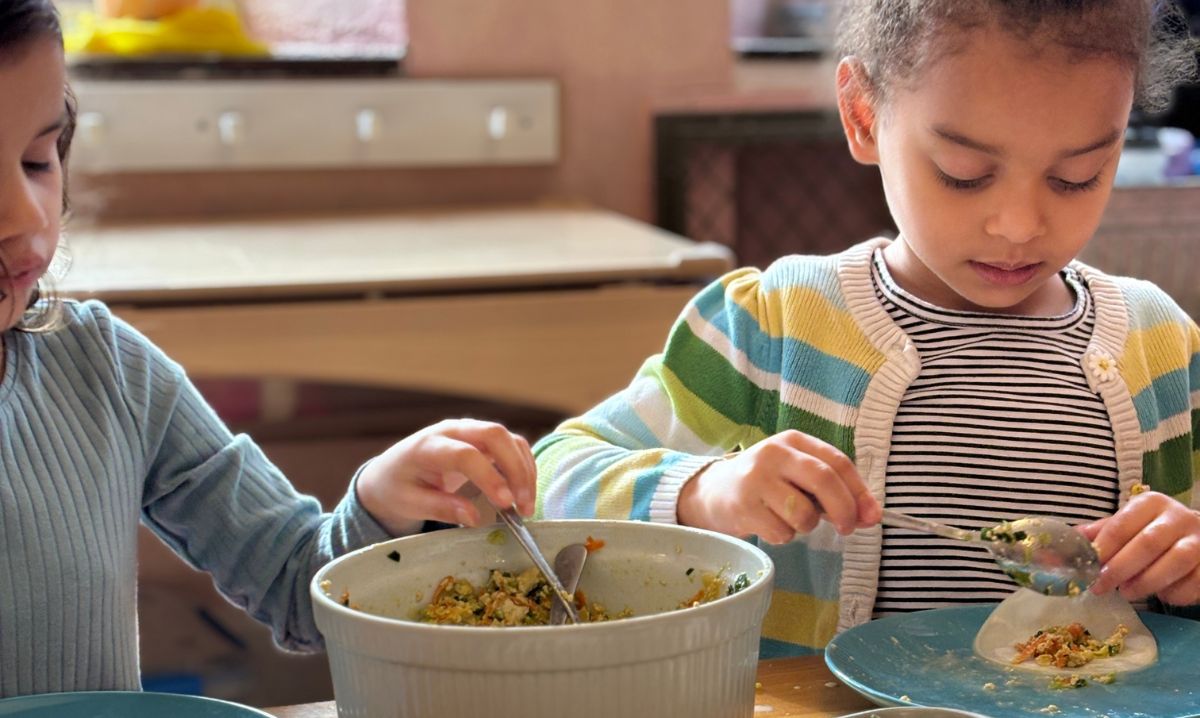 Two young children at Detroit Waldorf School participate in a hands-on cooking activity, carefully preparing food together in a classroom setting.