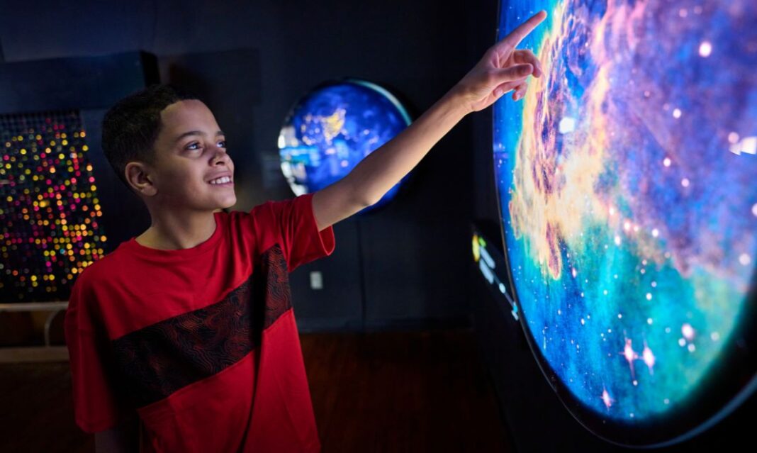 A young boy interacts with a colorful digital space exhibit at Impression 5 Science Center in Lansing, Michigan, engaging in a hands-on learning experience about astronomy.