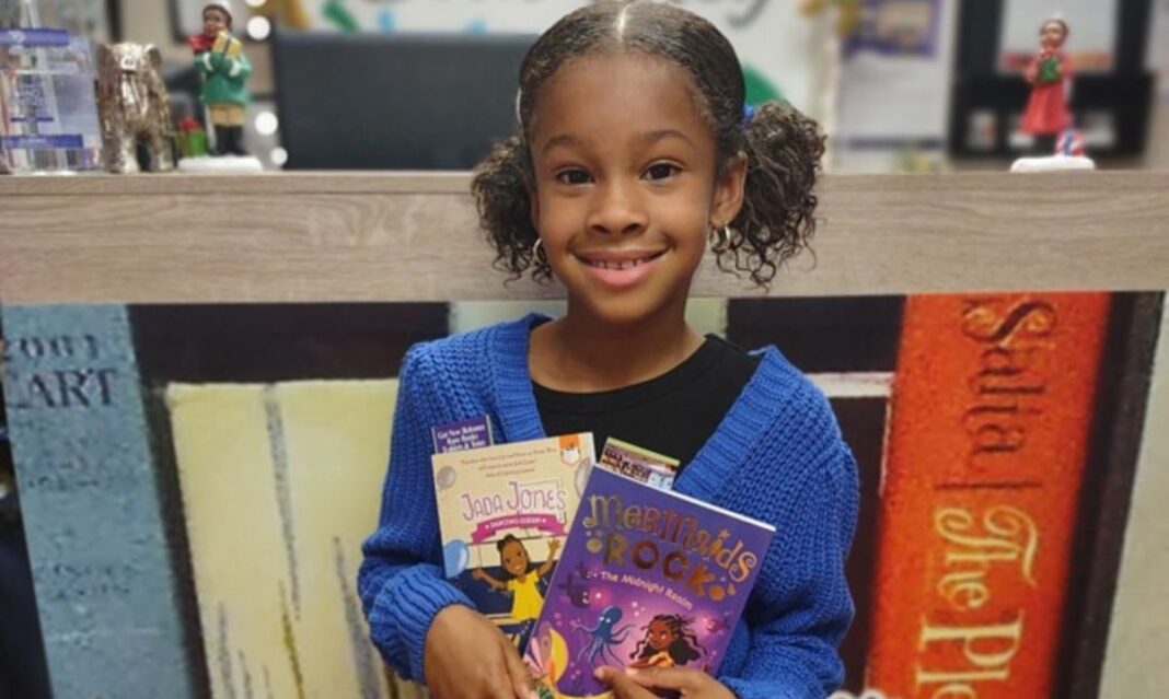 Young girl smiling and holding two children’s books, 