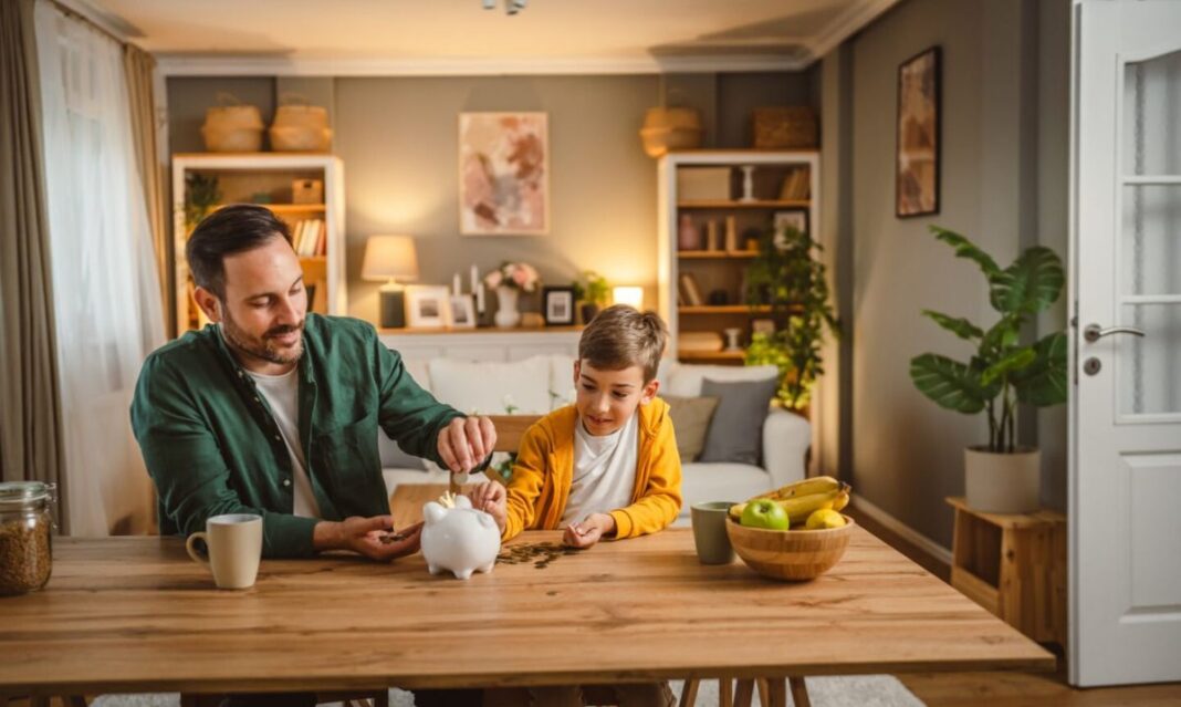 A father and son sitting at a wooden table, putting coins into a piggy bank, symbolizing family savings goals and financial planning.