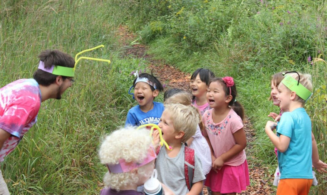Children laughing and playing outdoors at Leslie Science & Nature Center Summer Camps, participating in a fun nature-themed activity with a camp counselor.