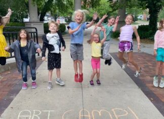 Excited kids jumping in the air at Art Explorers Summer Camp at Riverside Arts Center, with 'Art Camp!' written in colorful chalk on the sidewalk. A fun and creative summer camp experience for children.