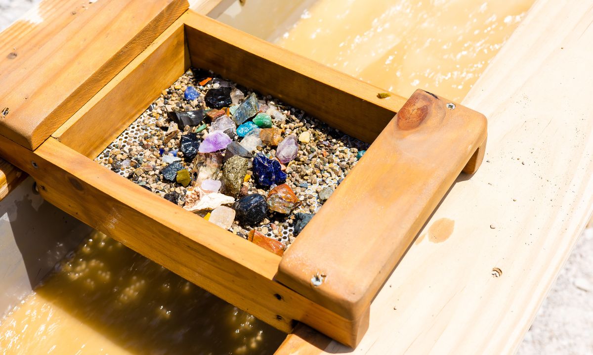 A wooden sifting tray filled with colorful gemstones and minerals at a gem mining attraction in Hocking Hills, Ohio, a fun hands-on activity for families and kids.