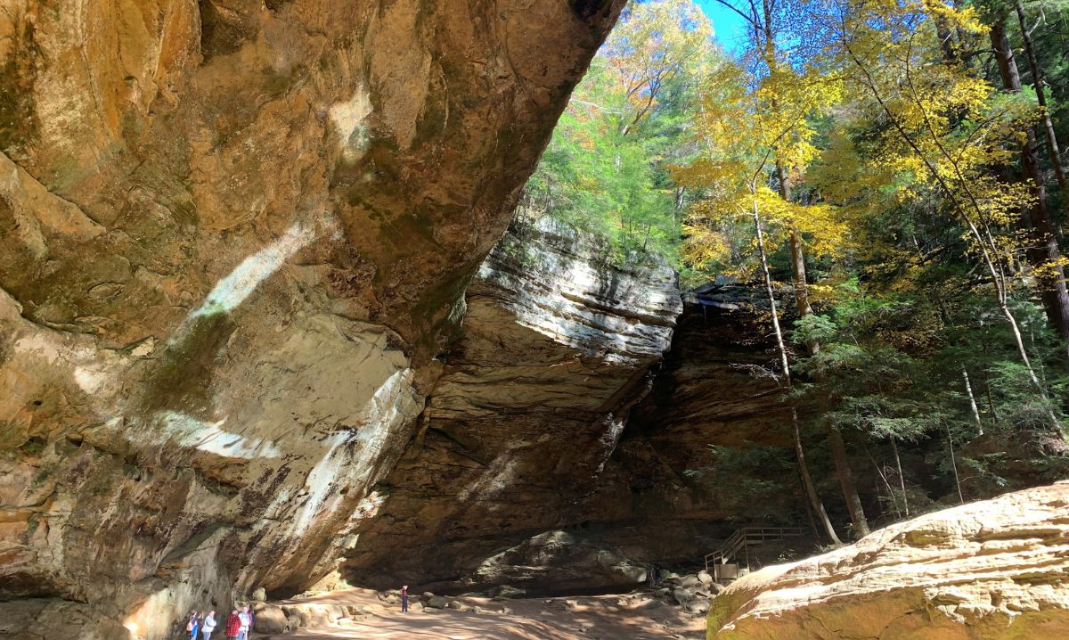 A stunning view of Old Man’s Cave in Hocking Hills, Ohio, with towering rock formations, vibrant fall foliage, and sunlight streaming through the trees, making it a perfect hiking destination.