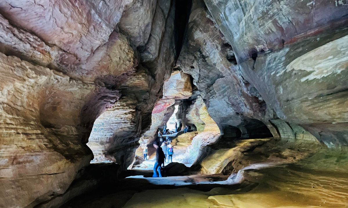 Visitors exploring Rock House Cave in Hocking Hills, Ohio, a unique tunnel-like sandstone cave featuring high ceilings, natural windows, and breathtaking rock formations, making it a popular hiking and sightseeing destination.