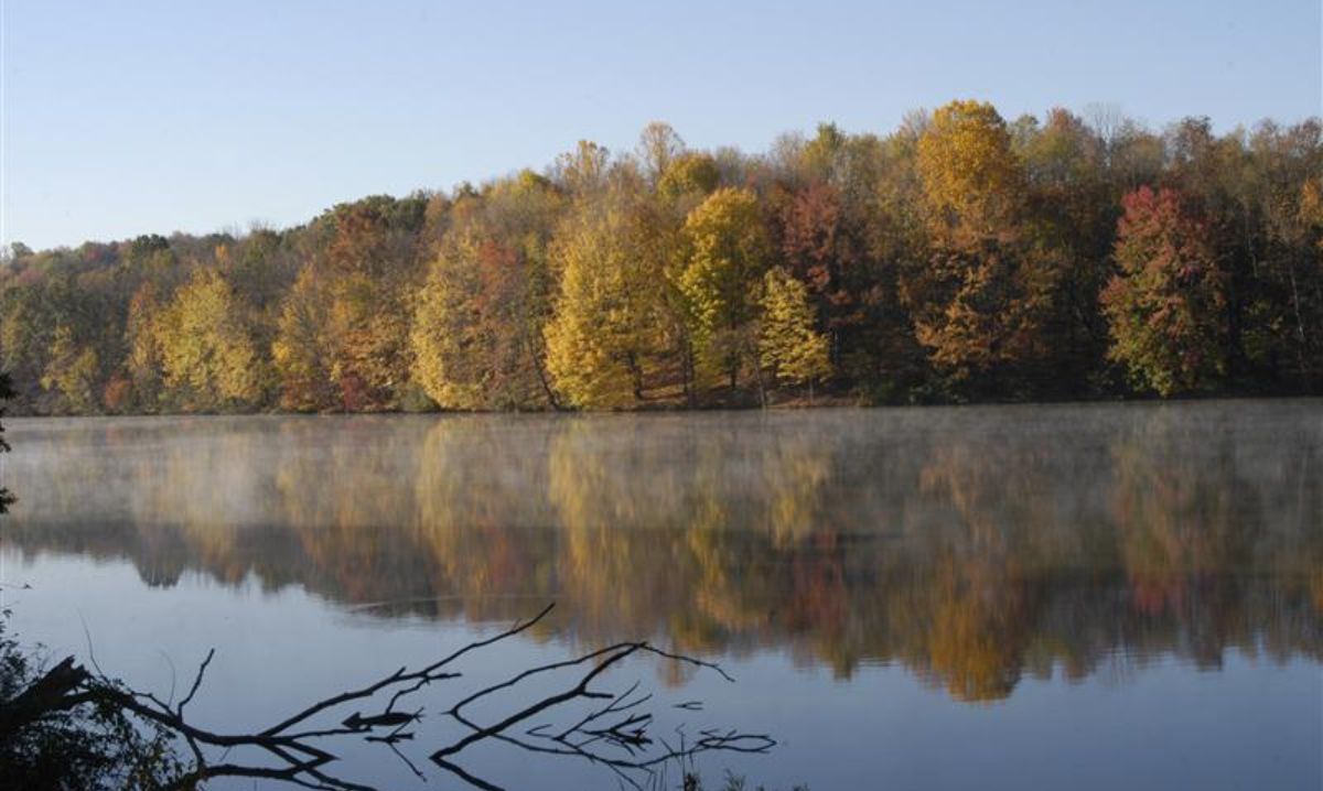 A serene lake in Hocking Hills, Ohio, reflecting the vibrant autumn foliage of surrounding trees, creating a picturesque fall landscape.